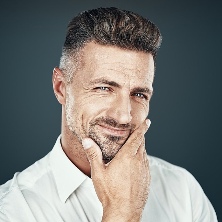 Pure confidence. Handsome young man smiling and looking at camera while standing against grey background